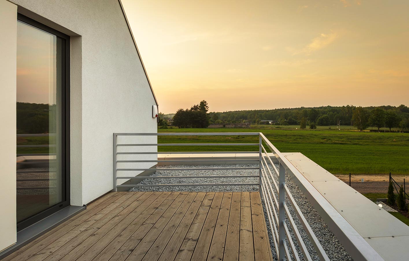 moderne Terrasse mit Geländer mit Blick ins Grüne und einem Sonnenaufgang
